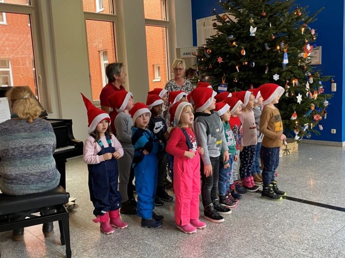 Ein Kinderchor wird von einer Frau am Piano begleitet